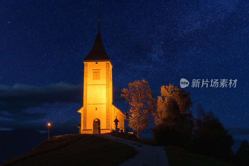 在斯洛文尼亚的山上，被照亮的Jamnik教堂St Primus和felian的风景。风景优美，星空湛蓝，户外旅游背景